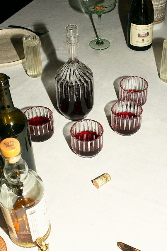 Photograph of four glasses of red wine, a carafe, on a white tablecloth...